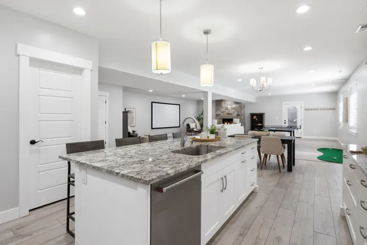 Full kitchen featuring light stone counters, a kitchen breakfast bar, dishwasher, white cabinets, and an island with sink