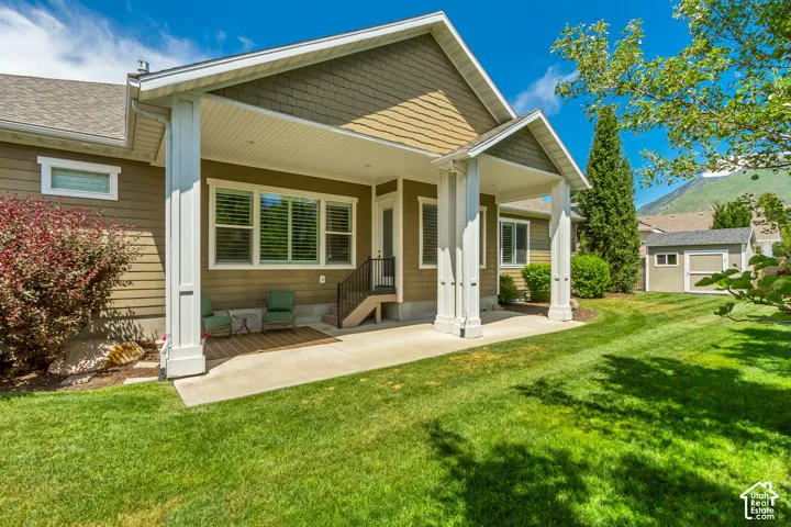 Expansive lawn with a covered patio, featuring substantial white support columns, a gray shingle roof, and a visible mountain backdrop