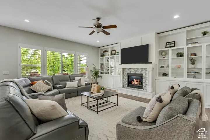 Living area featuring ceiling fan, wood finished floors, built in shelves, a glass covered fireplace, and recessed lighting
