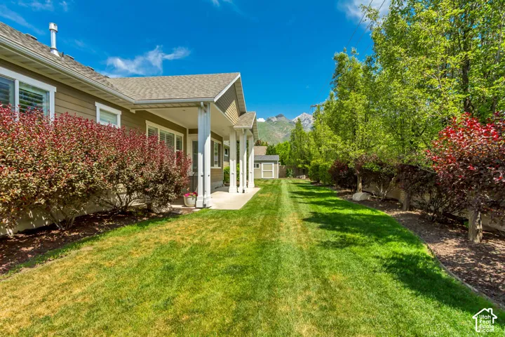 Spacious side yard featuring a manicured lawn, established shrubbery, and mature trees