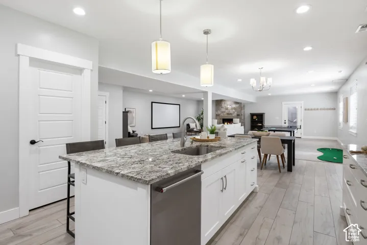 Full kitchen featuring light stone counters, a kitchen breakfast bar, dishwasher, white cabinets, and an island with sink