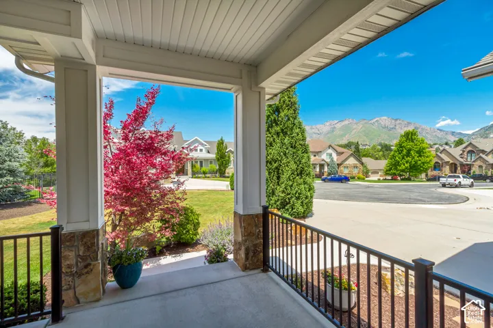 Covered porch featuring stone-clad pillars, a concrete surface, and black metal railings