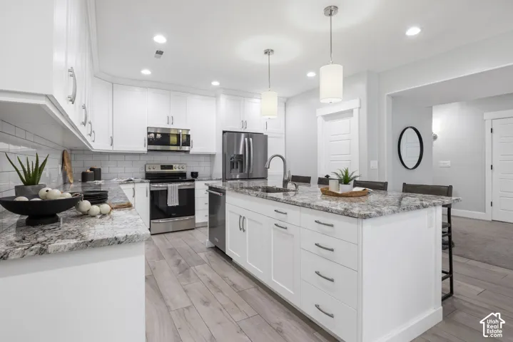 Full kitchen with light stone counters, white cabinetry, a kitchen bar, stainless steel appliances, and light wood finished floors