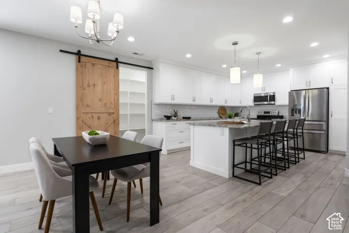 Kitchen featuring a pantry, stainless steel appliances, light stone counters, a kitchen breakfast bar, and white cabinetry