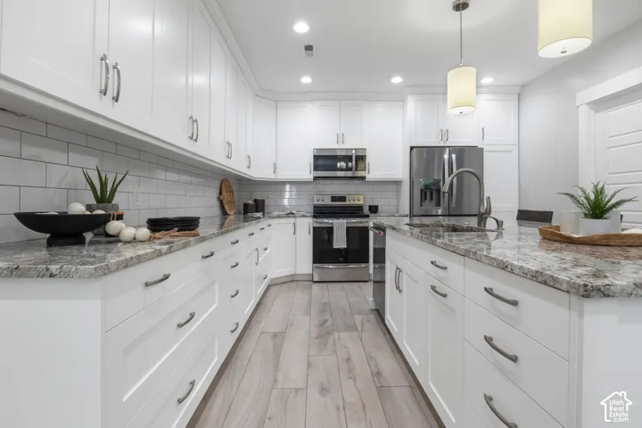 Full kitchen with white cabinets, light stone countertops, stainless steel appliances, and light wood-type flooring