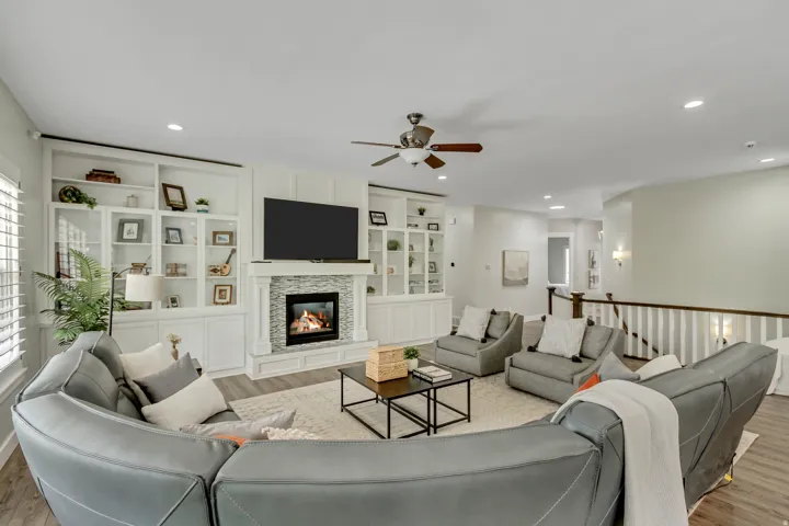 Living area featuring light wood-type flooring, a fireplace, ceiling fan, built in shelves, and recessed lighting