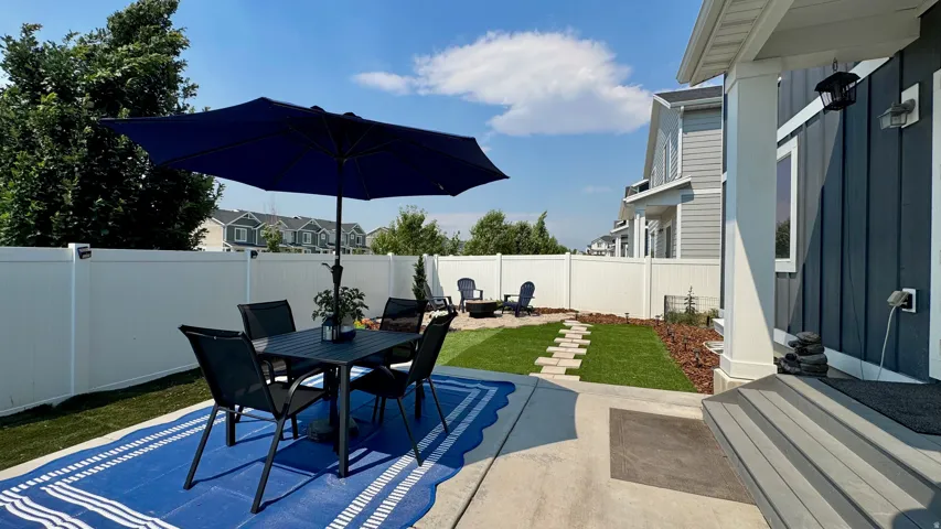 Expansive backyard featuring a white vinyl privacy fence, concrete patio, and segmented stone walkway