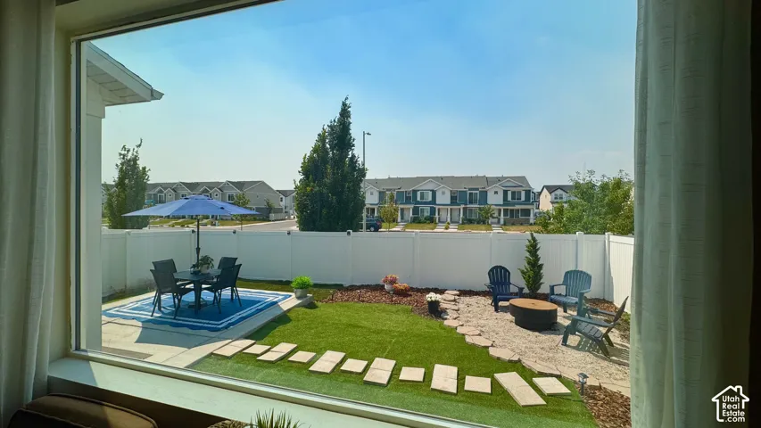 Fully fenced backyard featuring a paved patio area, artificial turf, and a stone-paved fire pit zone