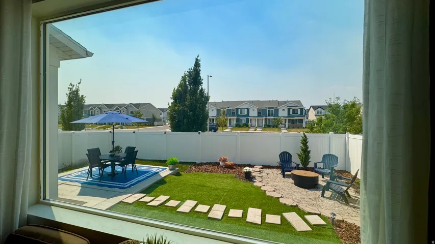 Fully fenced backyard featuring a paved patio area, artificial turf, and a stone-paved fire pit zone