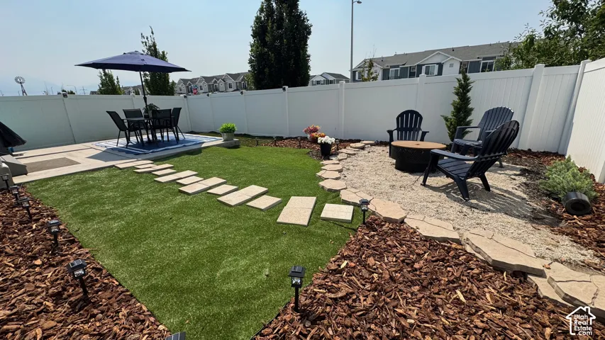 Private backyard featuring a paved patio, artificial turf lawn, and a gravel fire pit area