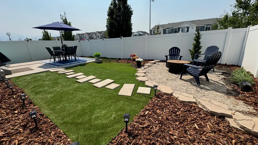 Private backyard featuring a paved patio, artificial turf lawn, and a gravel fire pit area