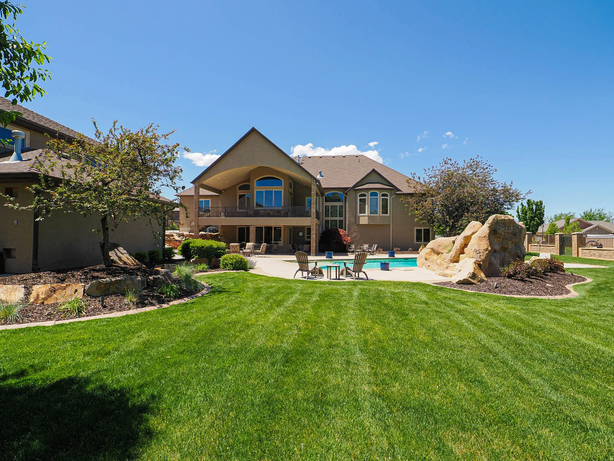 Expansive backyard featuring a large lawn, a swimming pool, and natural rock landscaping
