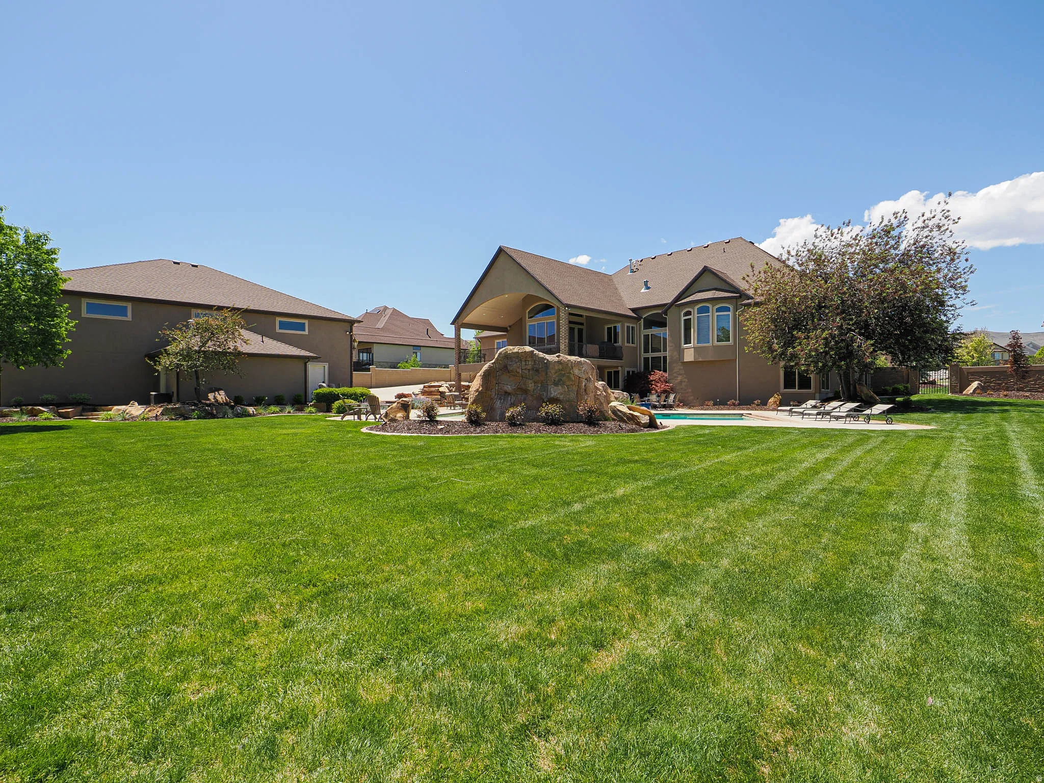 Spacious backyard featuring a large green lawn, a swimming pool with surrounding patio, and mature landscaping elements