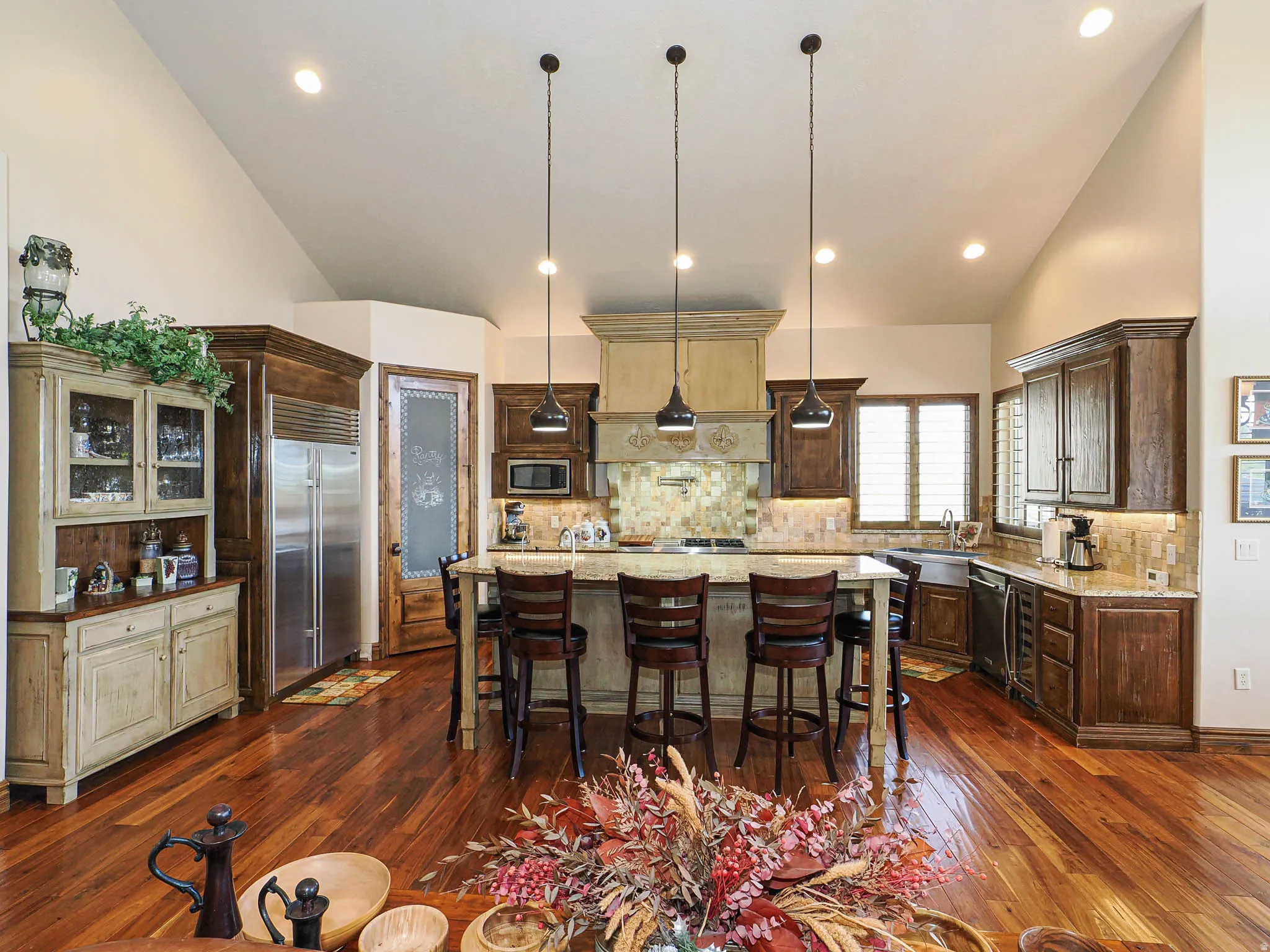 Kitchen featuring vaulted ceilings, wood-finish flooring, a central island with bar seating, stainless steel appliances, and a tile backsplash