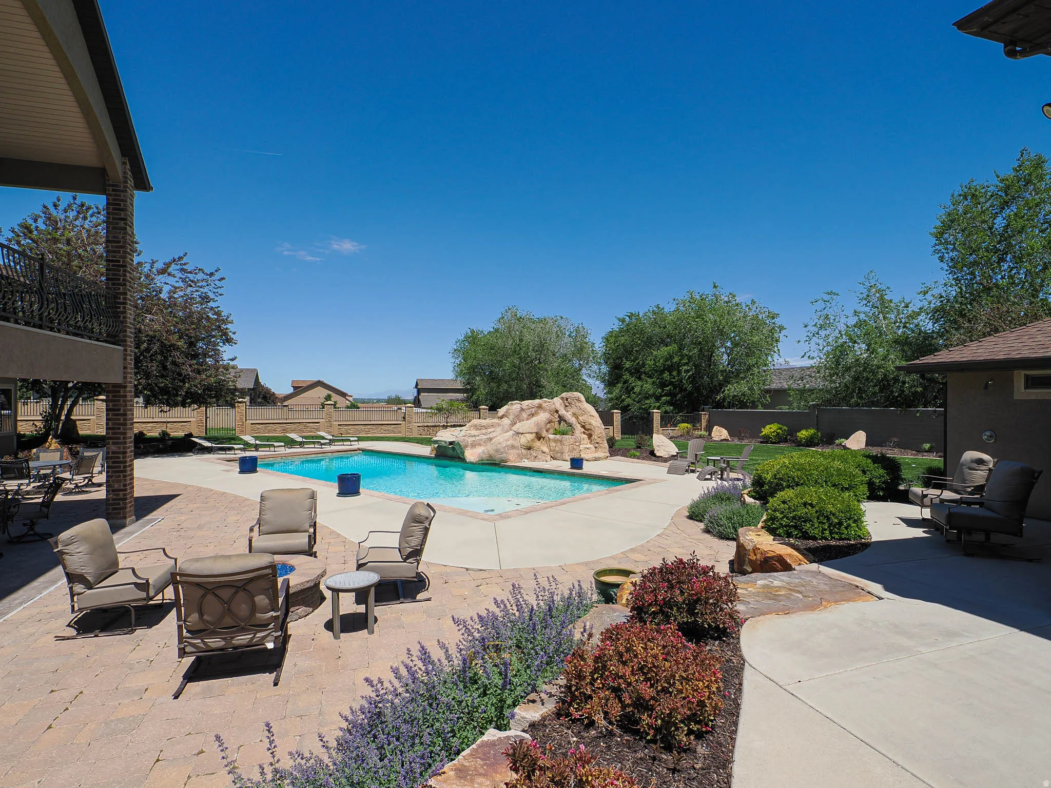 Expansive outdoor living area featuring a rectangular swimming pool with a rock water feature, surrounding concrete decking, and a multi-level paver patio