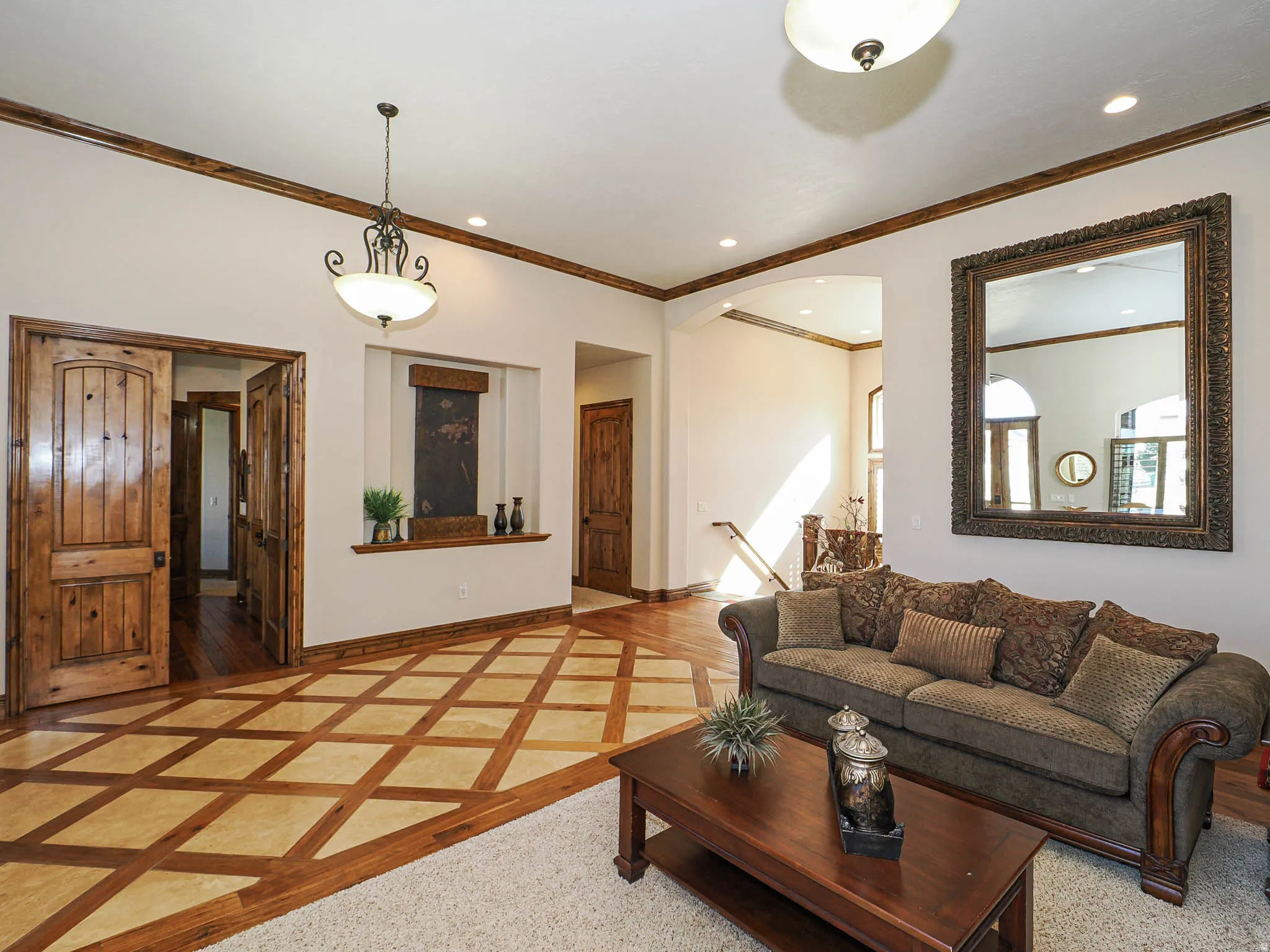 Living area featuring intricate wood-finish flooring with a diamond pattern, natural wood doors, and decorative crown molding