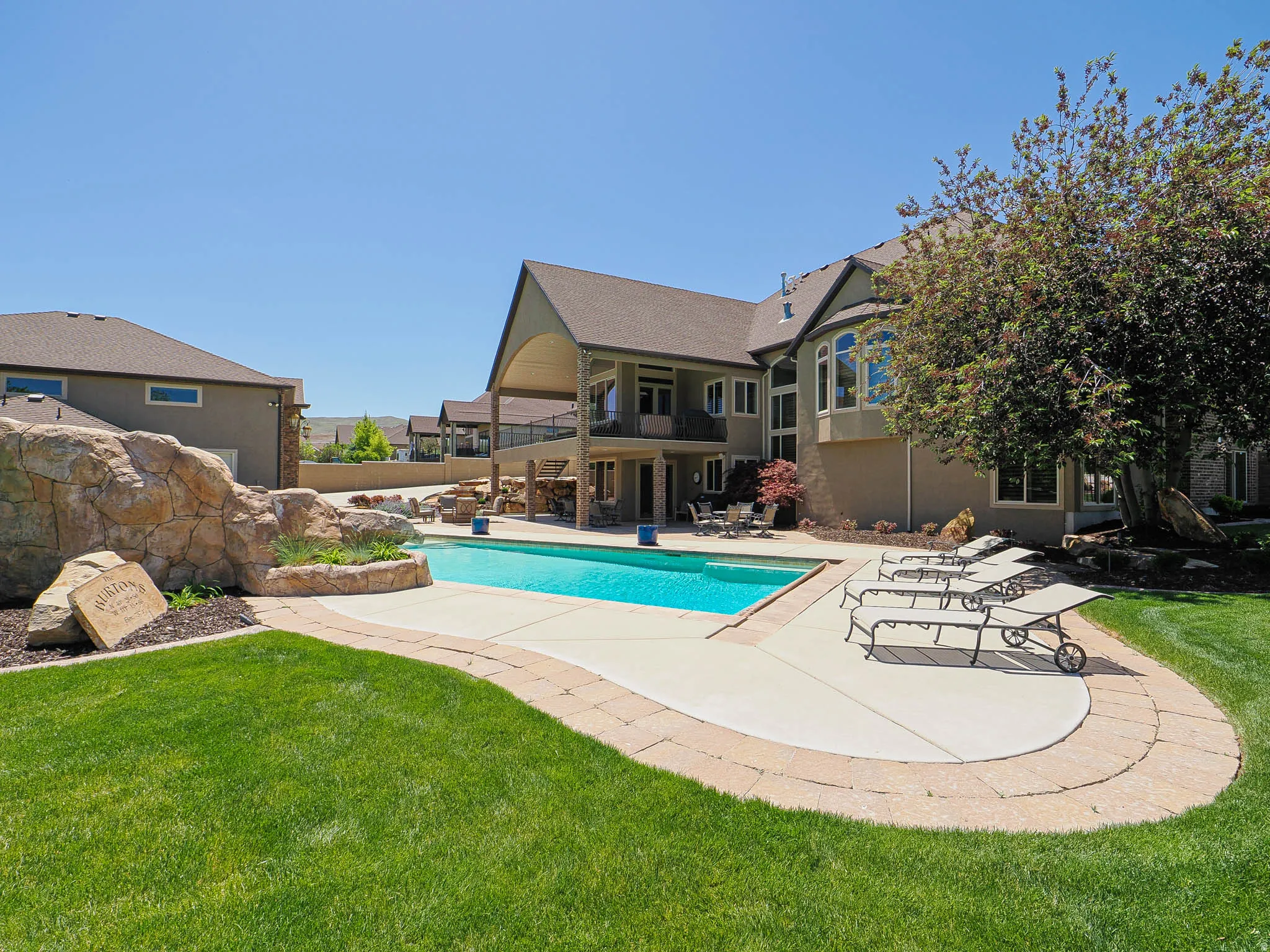 Expansive backyard featuring a custom-shaped swimming pool, decorative rock waterfall, paver-lined patio, and manicured lawn