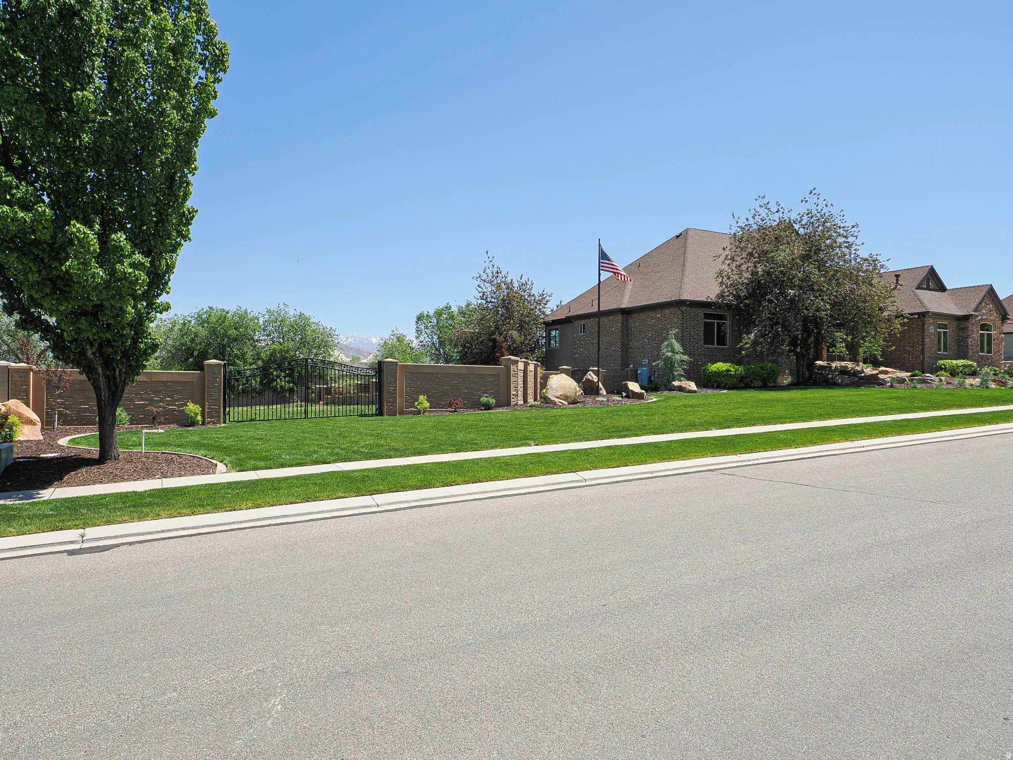 Expansive front lawn with mature trees and a decorative stone wall
