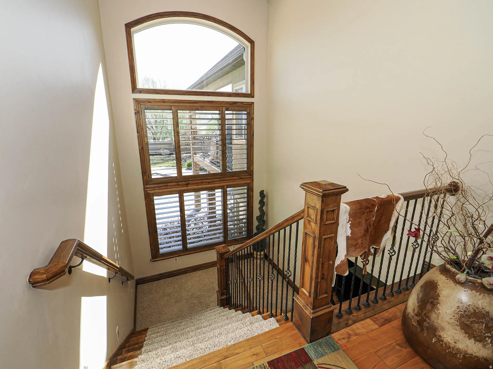 Stairwell featuring a tall window with an arched transom and wood-frame plantation shutters