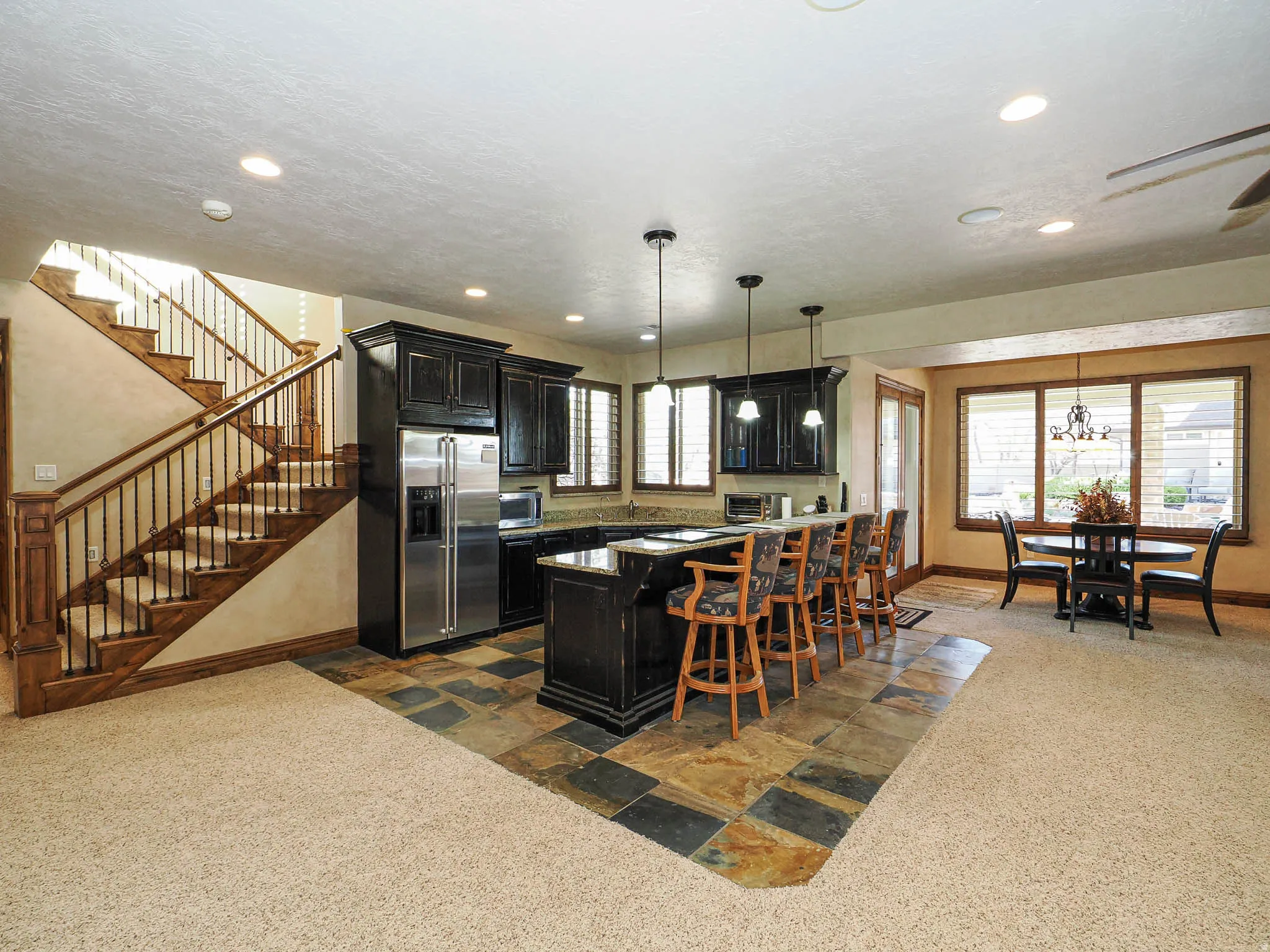 Open-concept living space featuring a U-shaped kitchen island with pendant lighting and built-in seating, stainless steel appliances, dark wood-finish cabinetry, and a dining area with window views