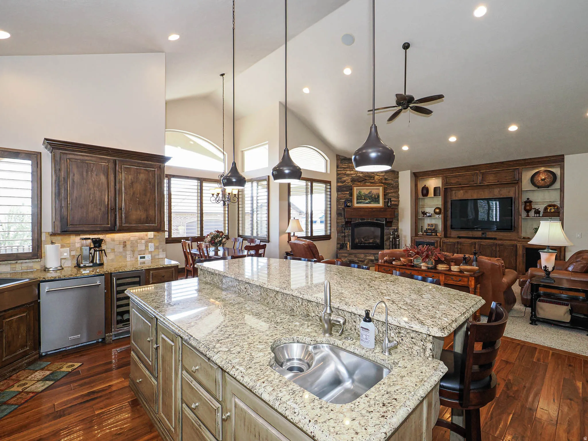 Spacious open-concept interior featuring a kitchen island with an undermount sink, granite countertops, and rich wood-finish flooring