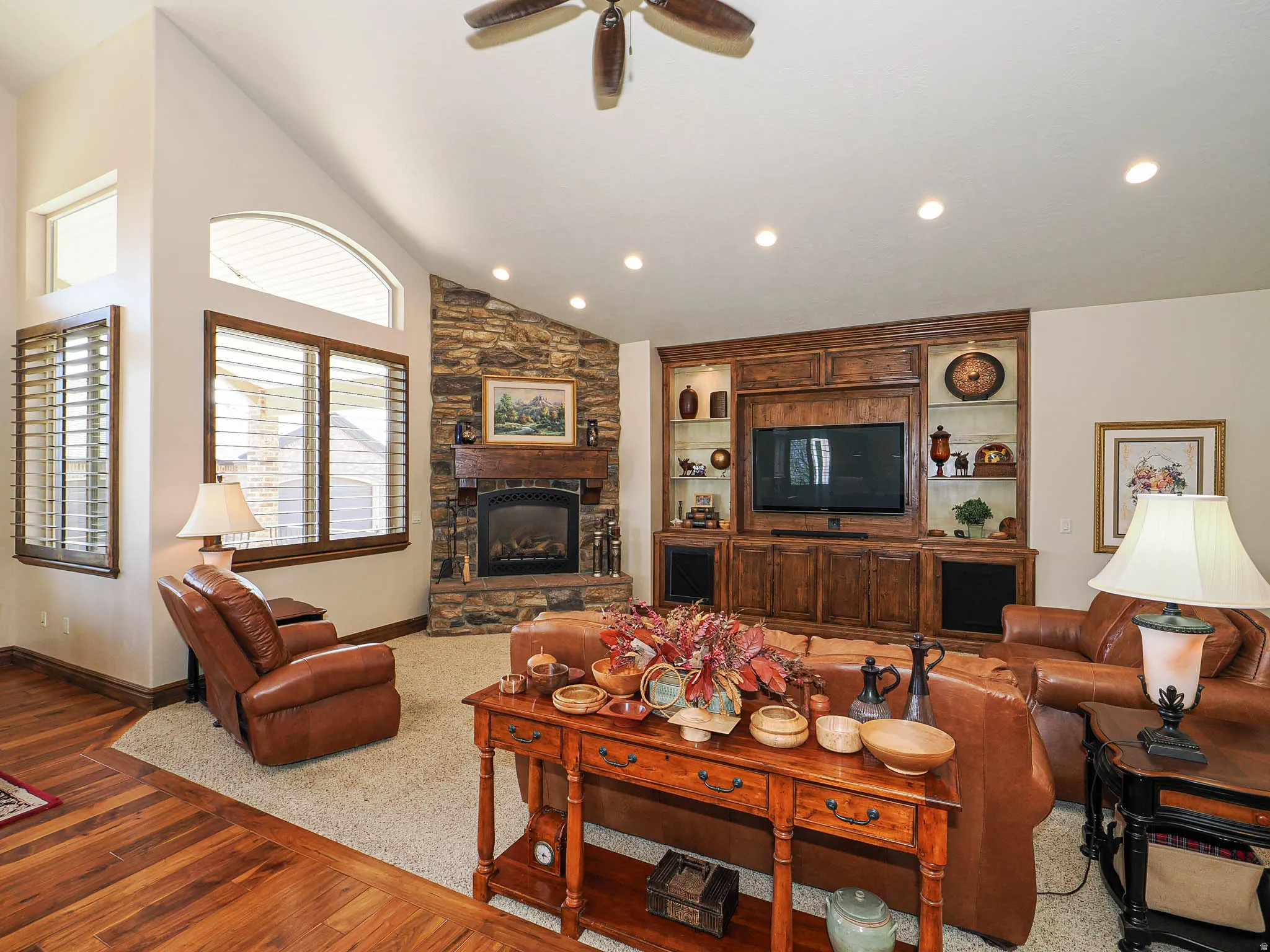 Spacious living area featuring a stone fireplace with a wood mantle, vaulted ceilings, and recessed lighting