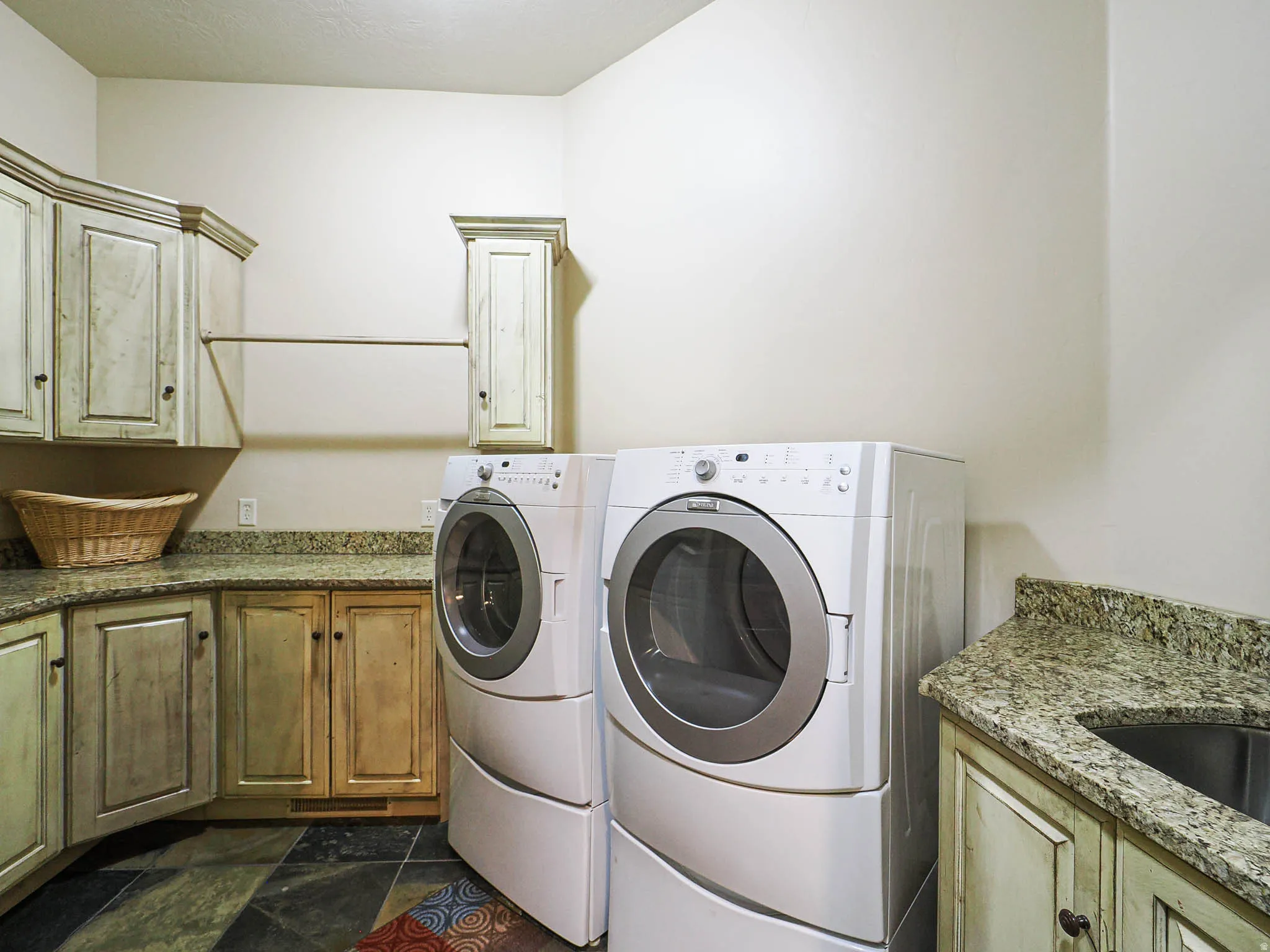 Laundry room featuring stacked washer and dryer, granite countertops, built-in cabinetry, and slate-style flooring