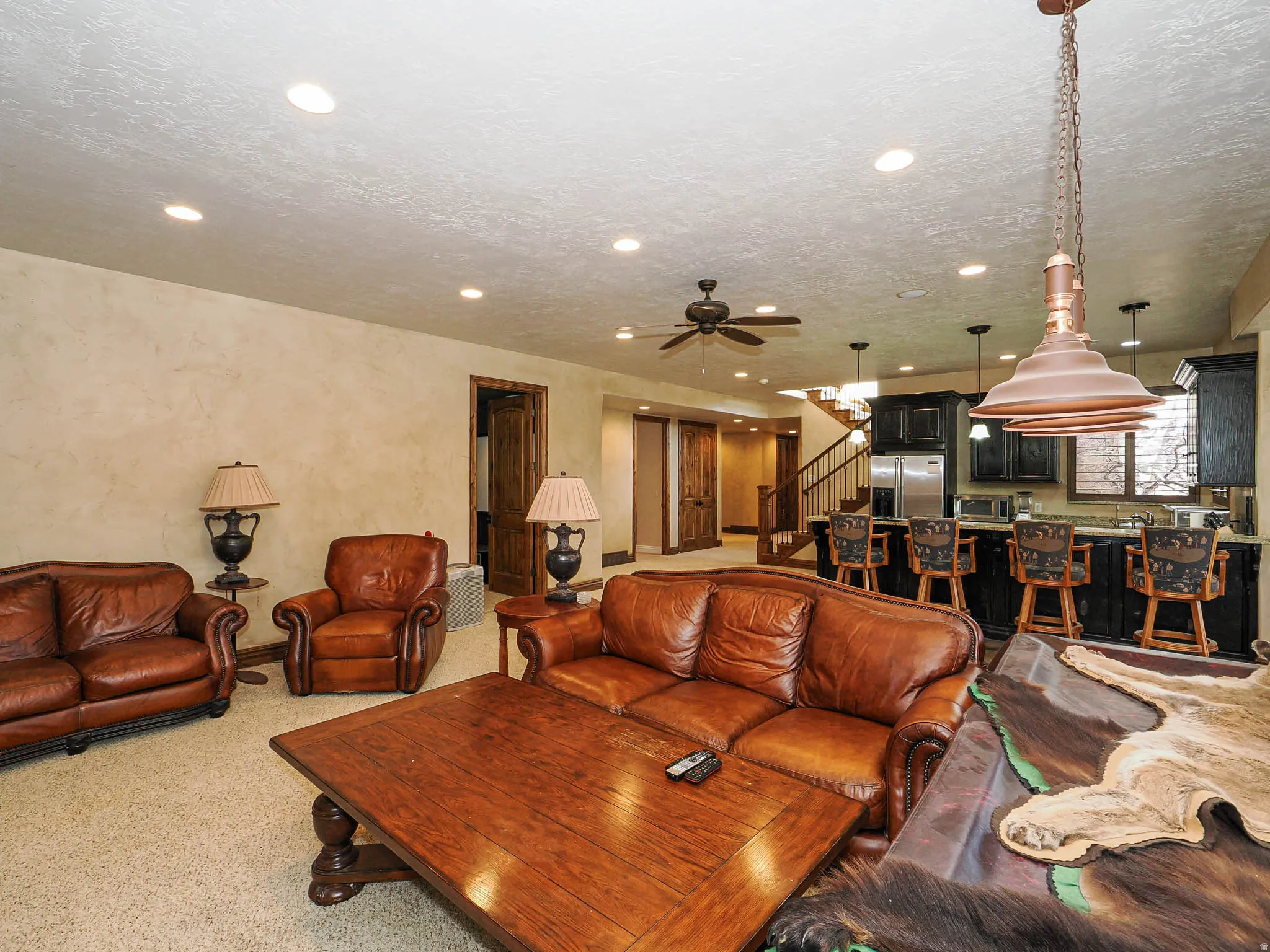 Spacious entertainment area featuring a wet bar with dark cabinetry, stainless steel refrigerator, and pendant lighting
