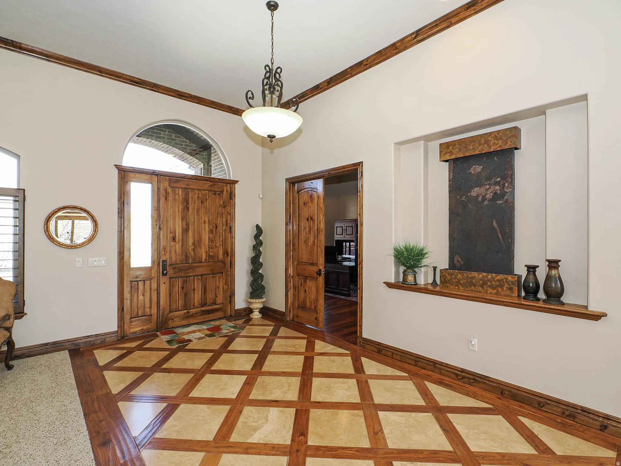 Entryway featuring custom wood-finish flooring with a diamond pattern, a grand wood-paneled door with an arched transom, and a built-in wall fountain with a slate-like finish