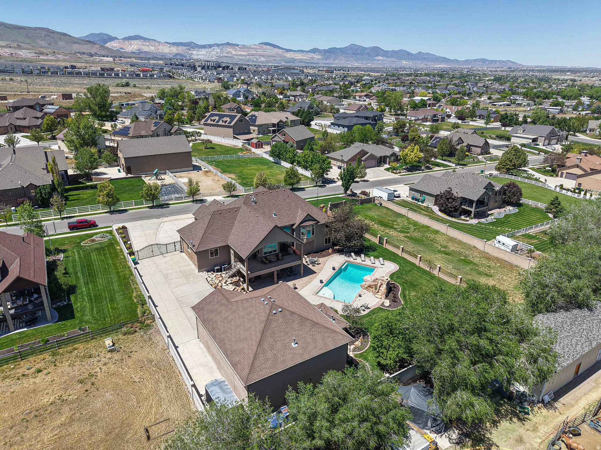 Spacious property featuring an inground swimming pool with rock detailing, extensive paved driveway, mature trees, and a multi-level deck