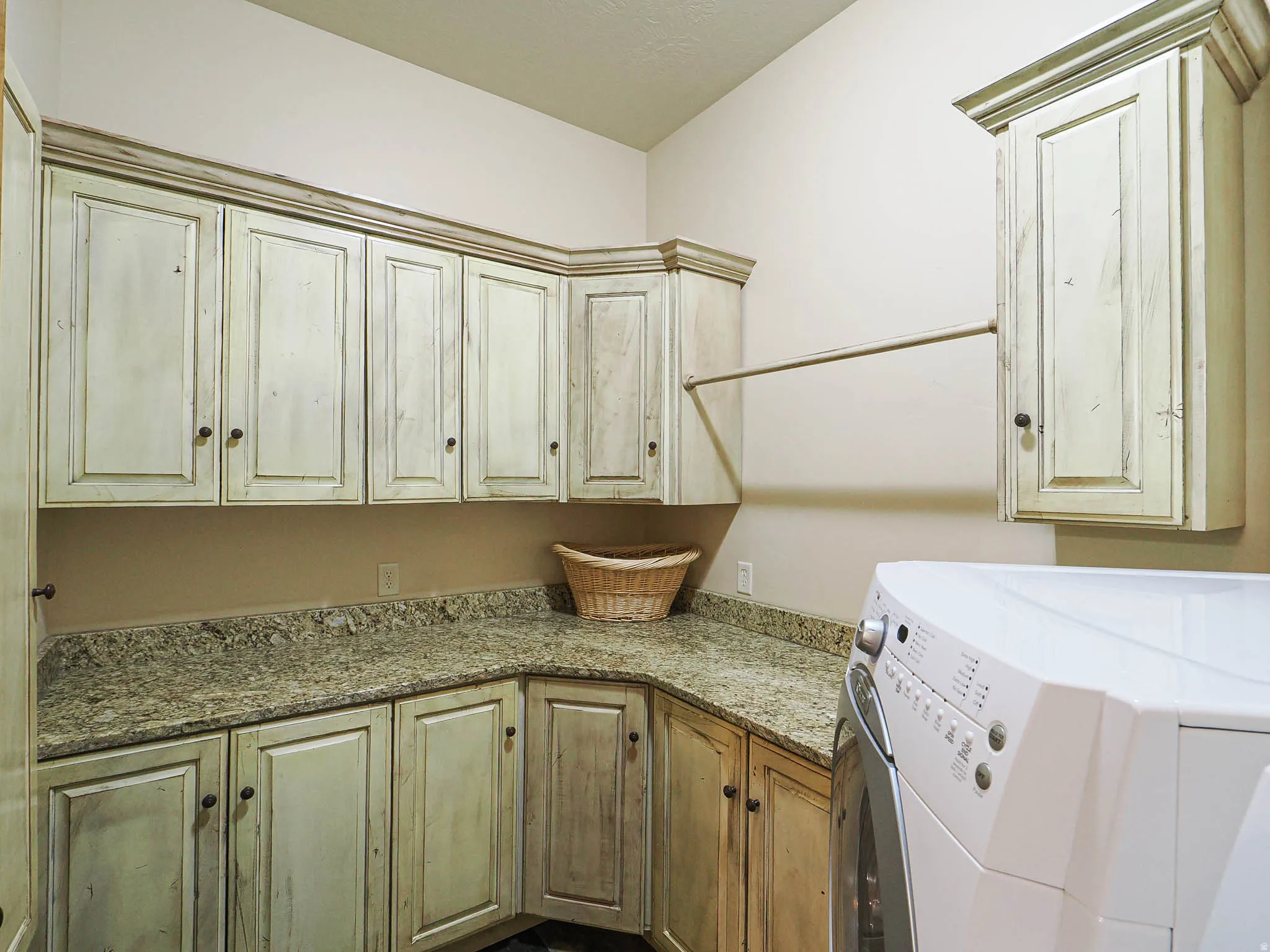 Laundry area featuring extensive cabinetry with a distressed finish, granite-style countertops, and a built-in hanging rod