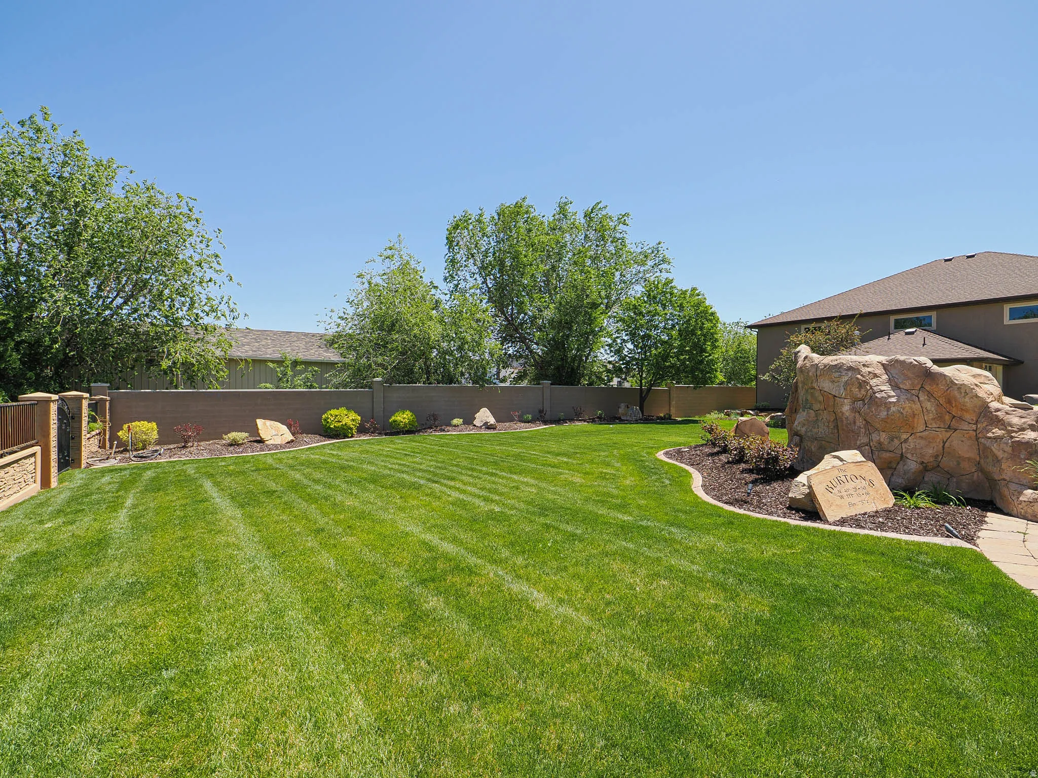 Expansive lawn with manicured landscaping, featuring a decorative stone formation, a stone paver pathway, and a perimeter wall