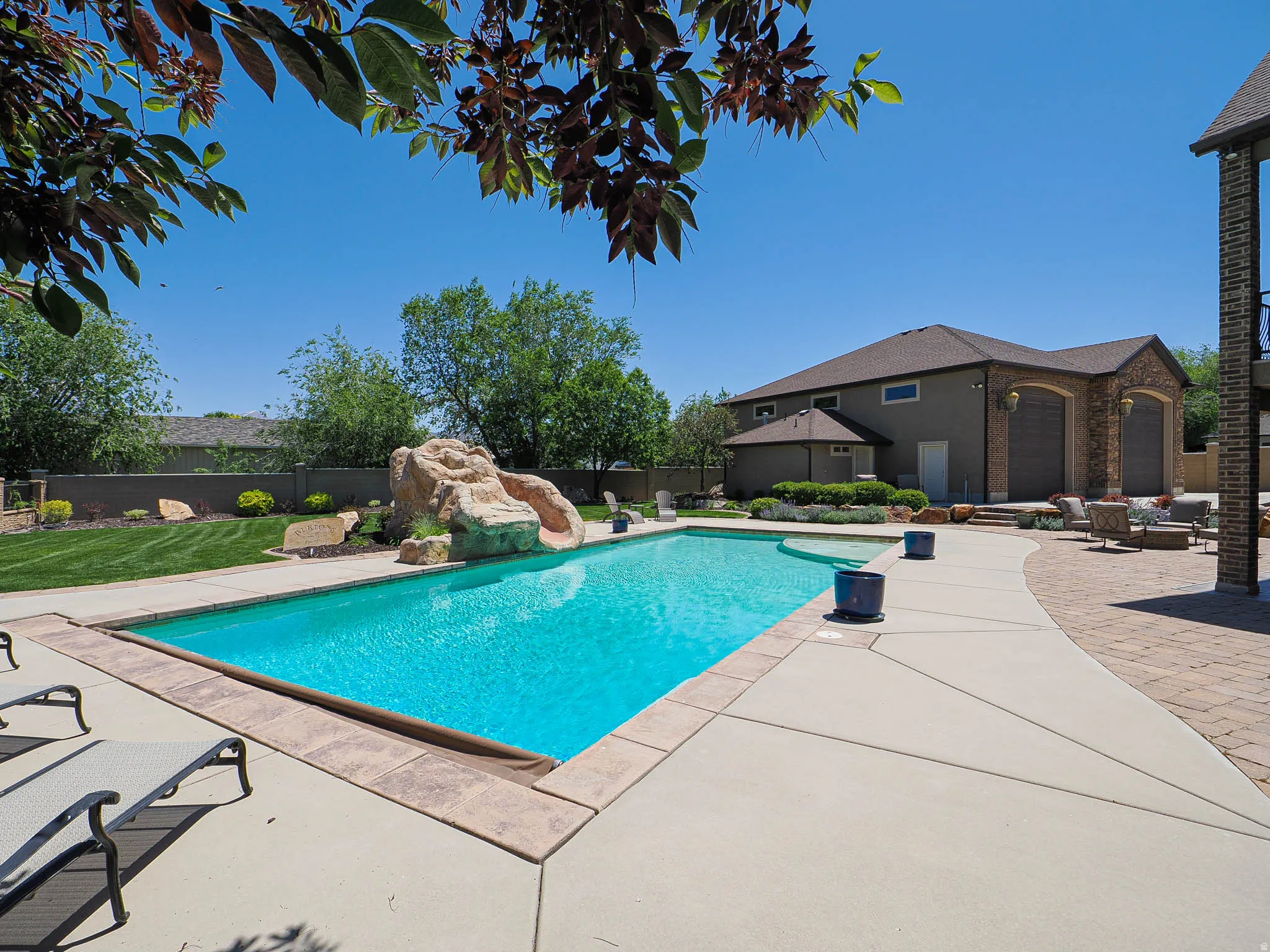 Outdoor aquatic area featuring a swimming pool with a rock slide, an expansive concrete patio, and a separate paved brick patio