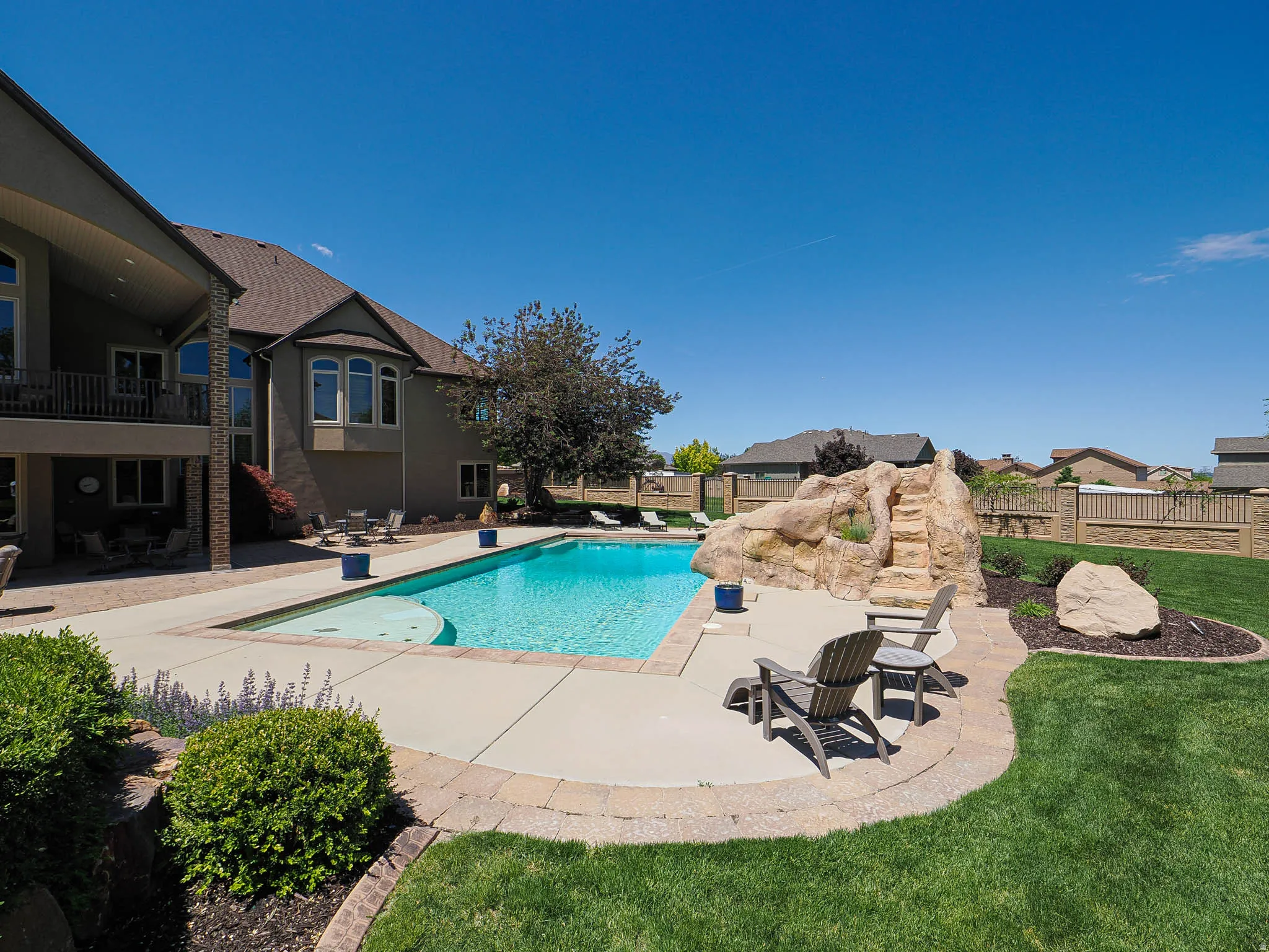 Expansive backyard featuring an in-ground swimming pool with a rock water feature, concrete pool deck, and surrounding landscaped lawn