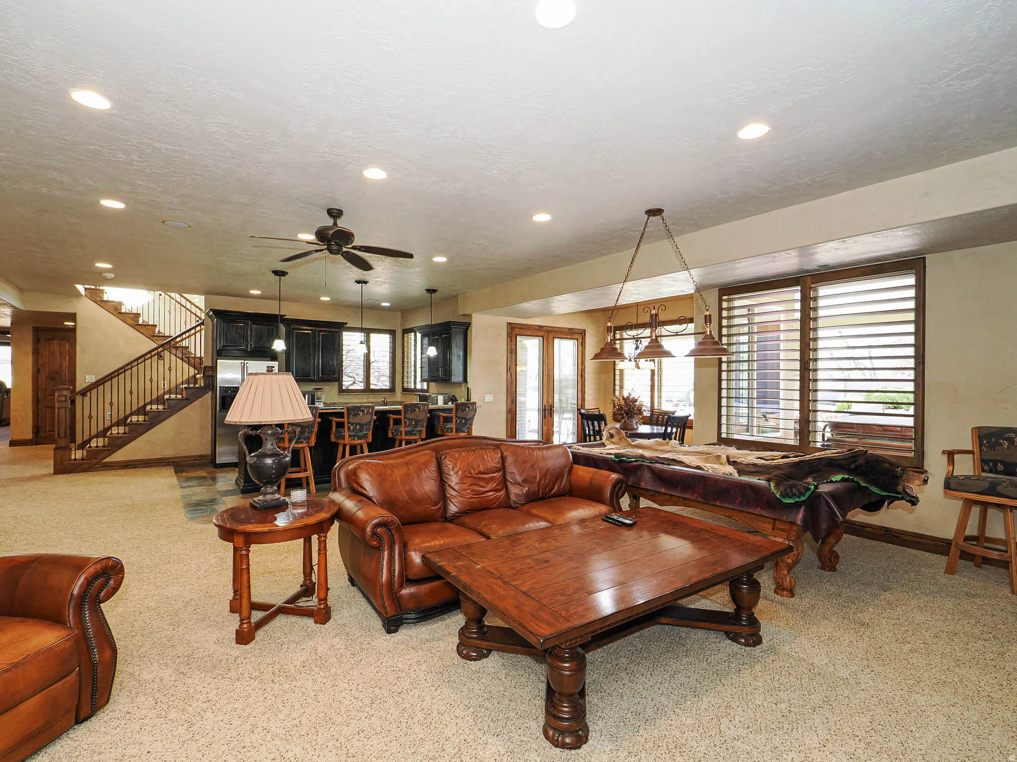 Spacious recreation room featuring carpet flooring, recessed lighting, a ceiling fan, and a built-in wet bar with dark cabinetry