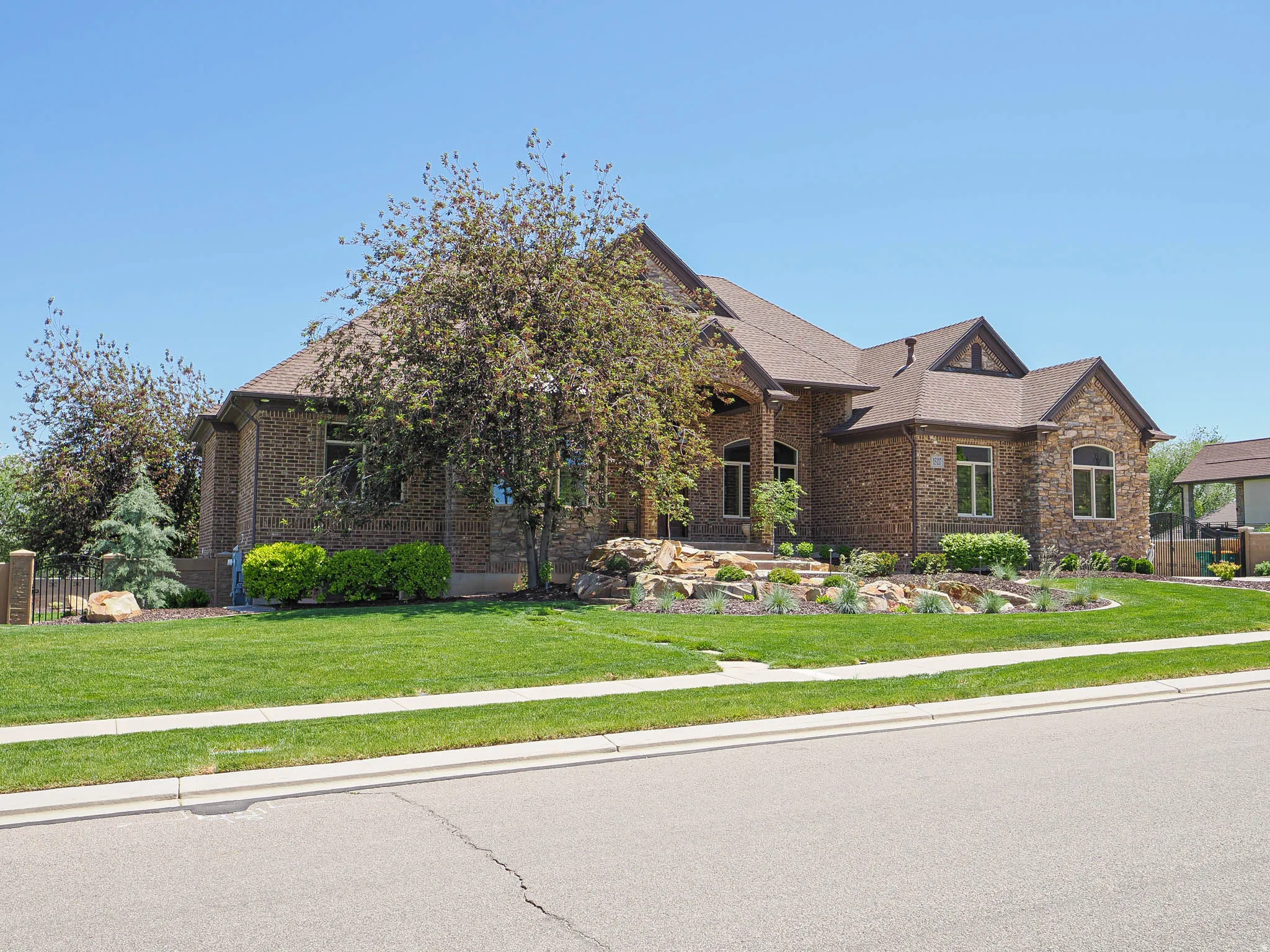 Stone and brick facade residence featuring a multi-gabled roofline, arched entry, mature landscaping, and an expansive lawn