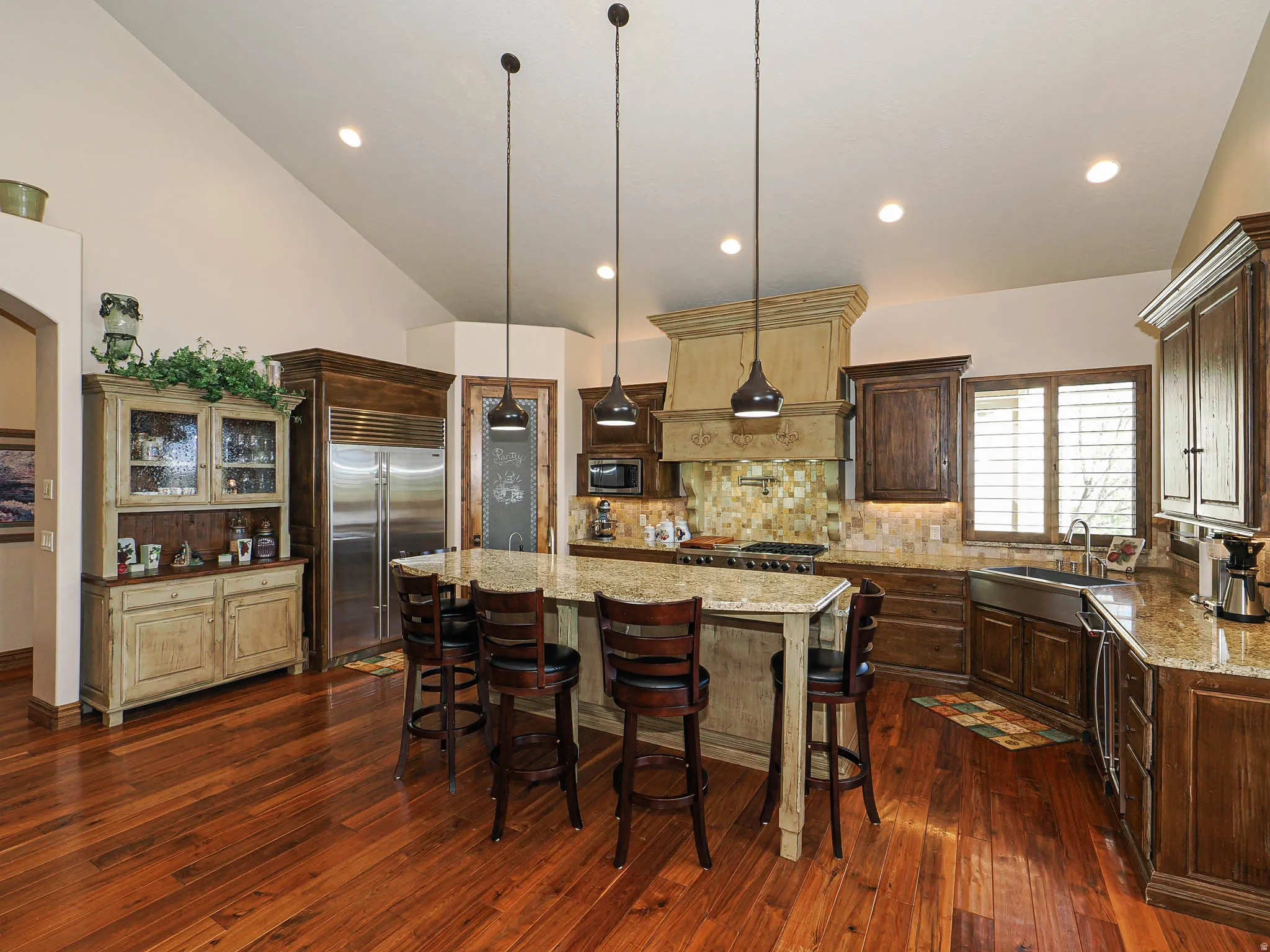 Kitchen featuring wood-finish flooring, a large central island with seating, granite countertops, stainless steel appliances, and a tile backsplash