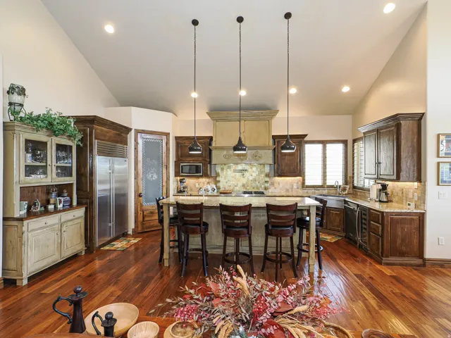 Kitchen featuring vaulted ceilings, wood-finish flooring, a central island with bar seating, stainless steel appliances, and a tile backsplash