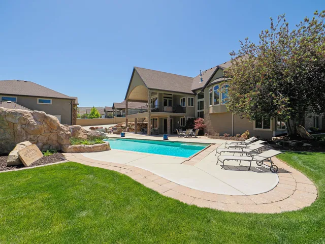 Expansive backyard featuring a custom-shaped swimming pool, decorative rock waterfall, paver-lined patio, and manicured lawn