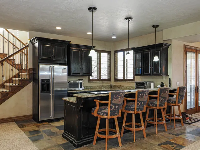 Kitchenette featuring dark wood cabinetry, a built-in stainless steel refrigerator, granite countertops, and three pendant lights illuminating the bar area