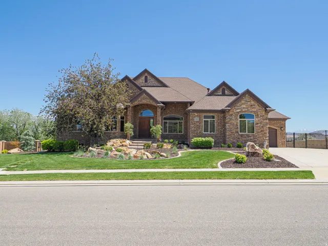 Stone facade residence featuring a large arched entryway with a wood door, multiple gabled rooflines, a concrete driveway, and established front yard landscaping with decorative rocks