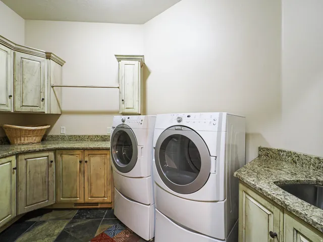 Laundry room featuring stacked washer and dryer, granite countertops, built-in cabinetry, and slate-style flooring