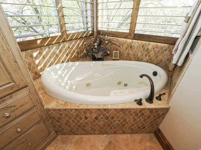 Soaking tub with bronze fixtures, mosaic tile surround, and plantation shutters