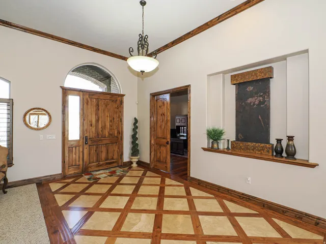 Entryway featuring custom wood-finish flooring with a diamond pattern, a grand wood-paneled door with an arched transom, and a built-in wall fountain with a slate-like finish