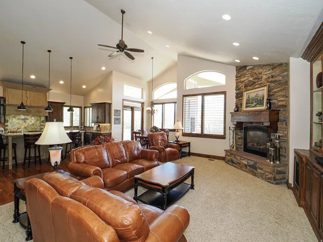 Spacious living area featuring a stacked stone fireplace with a substantial wood mantel, vaulted ceilings, and recessed lighting