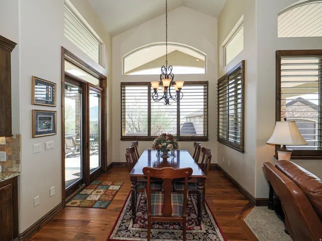 Vaulted ceiling dining area featuring hardwood flooring, extensive window treatments, and a glass-paneled patio door