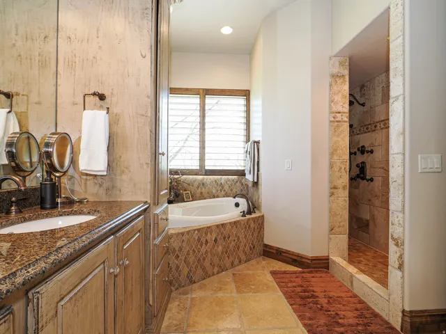 Bathroom featuring a corner soaking tub, a walk-in shower with stone tile, and a double vanity with stone countertops and distressed wood-finish cabinetry
