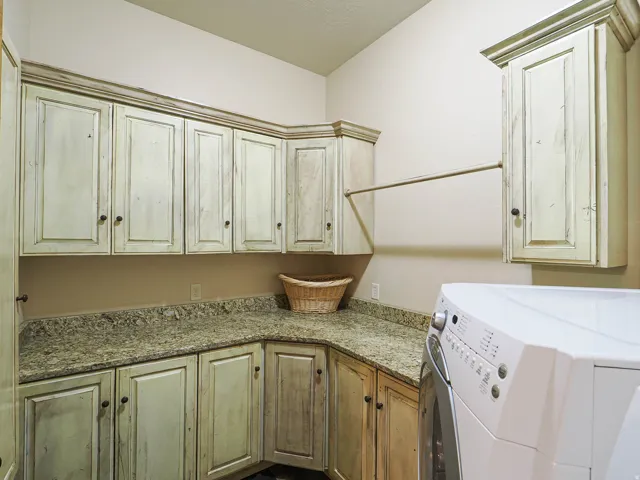 Laundry area featuring extensive cabinetry with a distressed finish, granite-style countertops, and a built-in hanging rod