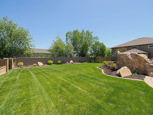 Expansive lawn with manicured landscaping, featuring a decorative stone formation, a stone paver pathway, and a perimeter wall
