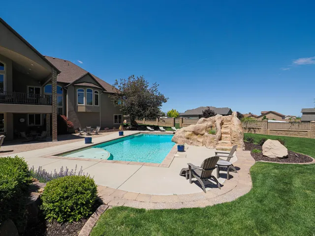 Expansive backyard featuring an in-ground swimming pool with a rock water feature, concrete pool deck, and surrounding landscaped lawn
